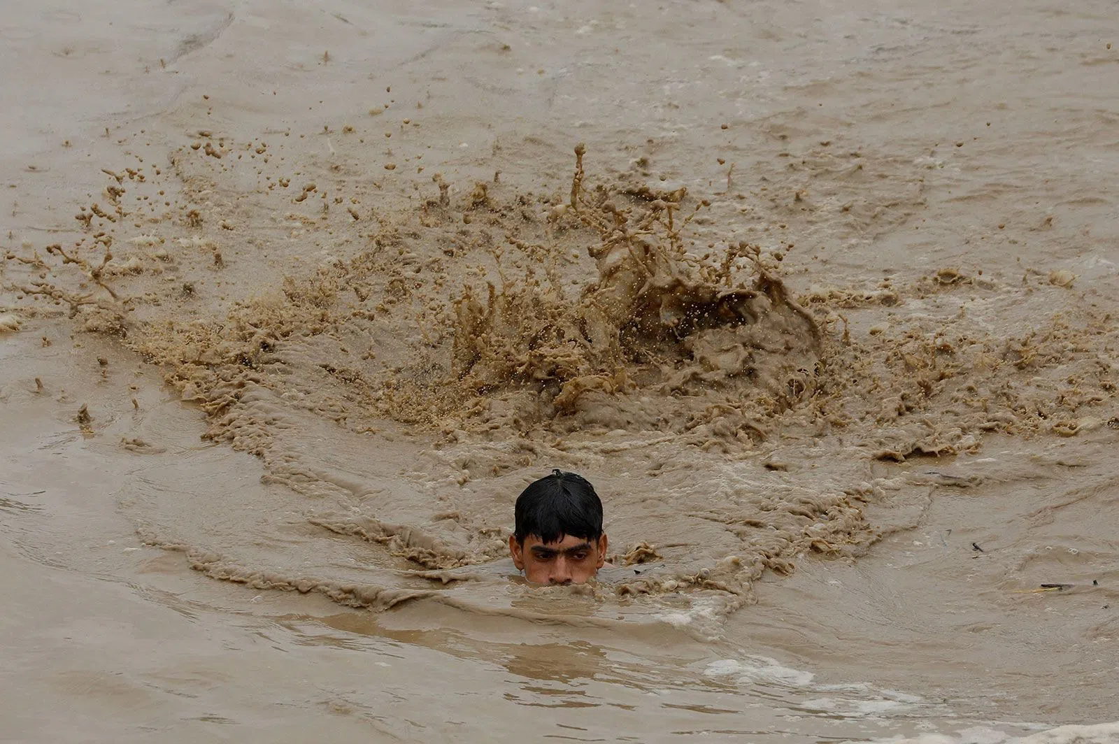 Người đàn ông bơi trong nước lũ đến vùng đất cao hơn ở  Charsadda, Pakistan, ngày 27/8. Ảnh: Reuters