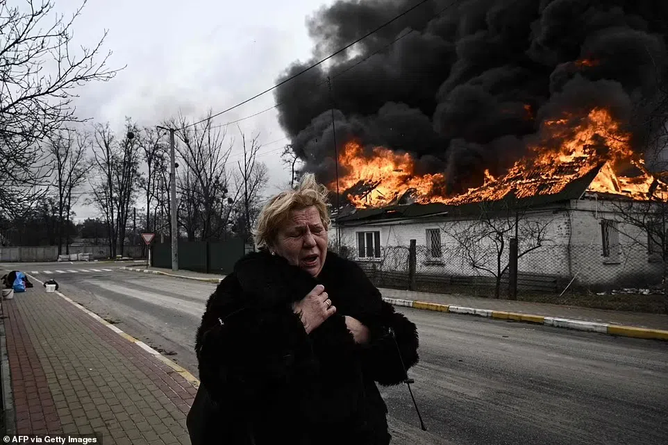 Một người phụ nữ khóc khi đứng trước ngôi nhà đang bốc cháy sau khi bị đổ vỏ ở thành phố Irpin, ngoại ô Kiev.