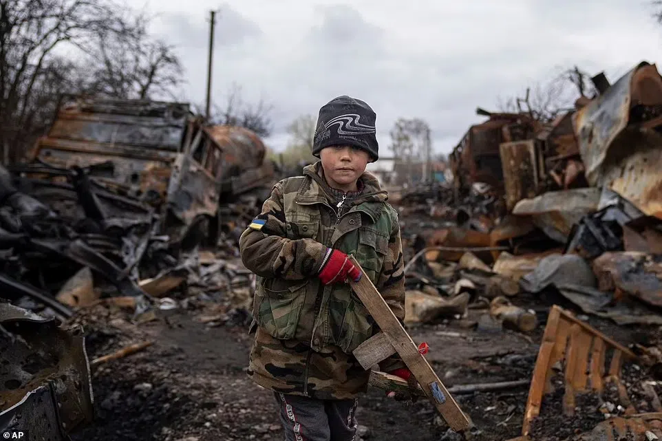 Yehor, 7 tuổi, cầm một khẩu súng trường đồ chơi bên cạnh các phương tiện quân sự bị phá hủy của Nga gần Chernihiv, Ukraine.