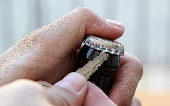 Cầm chắc chai bằng một tay, tay còn lại dùng chìa khóa đẩy phần lưỡi vào dưới mép nắp chai, rồi xoay chìa theo hướng bật máy xe.