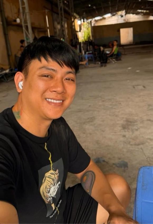 Anh diện áo phông đen, quần short đơn giản, ngồi trên ghế nhựa trong một không gian khá tuềnh toàng.