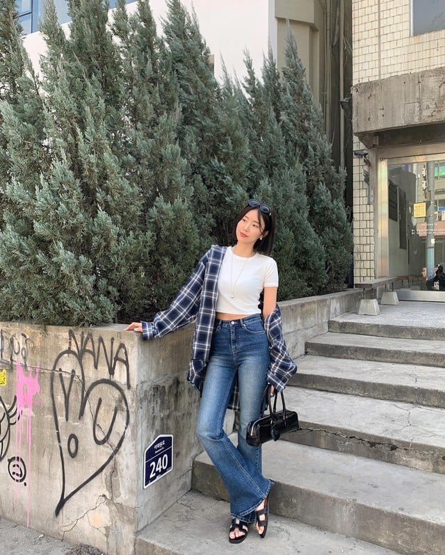 Set layer gồm áo thun trắng lửng, quần jeans và sơ mi kẻ ô khoác ngoài phù hợp không khí mùa thu.
