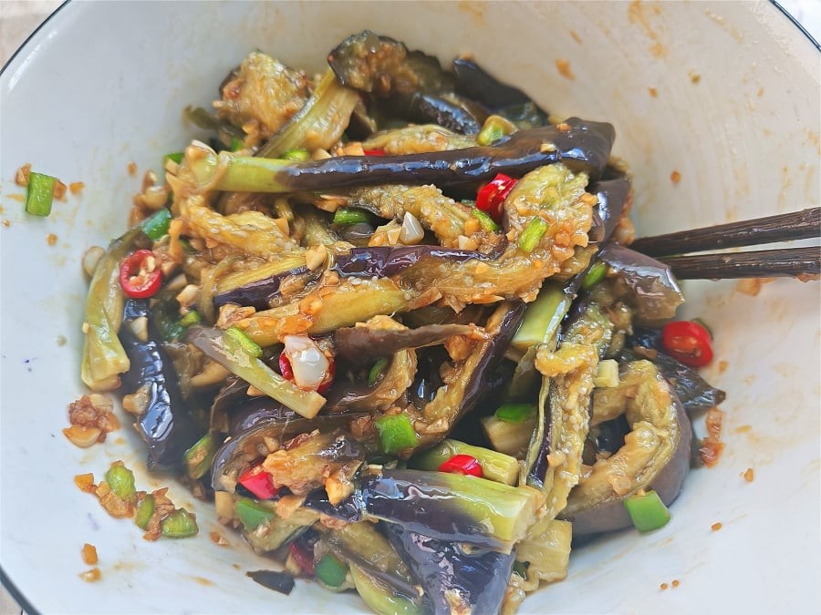 Cà tím sau khi hấp chín, được xé nhỏ và trộn cùng nước sốt cay nồng từ tỏi và ớt – từng sợi cà mềm thơm, thấm đẫm gia vị.