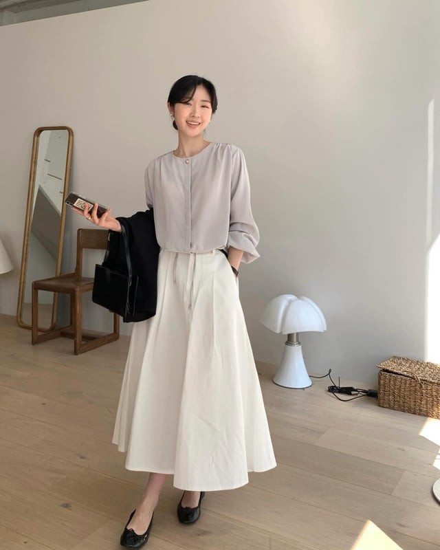 Áo blouse dài tay màu pastel phối cùng chân váy trắng chữ A tạo nên tổng thể nhẹ nhàng, duyên dáng. 