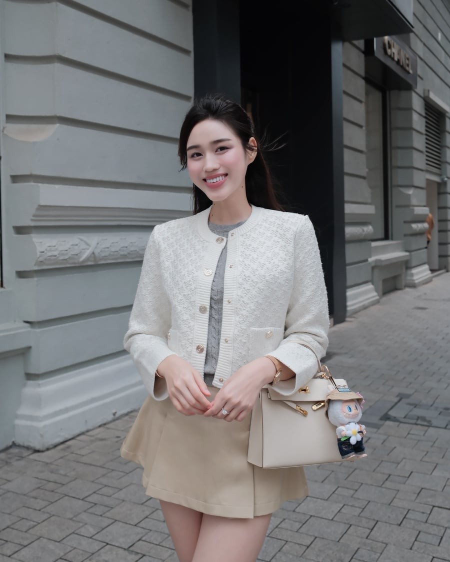 Với cardigan trắng và chân váy màu be, cô xây dựng hình ảnh ngọt ngào, mềm mại. Khi khoác thêm áo len xám, tổng thể được cân bằng, thêm phần sang trọng mà vẫn hài hòa.