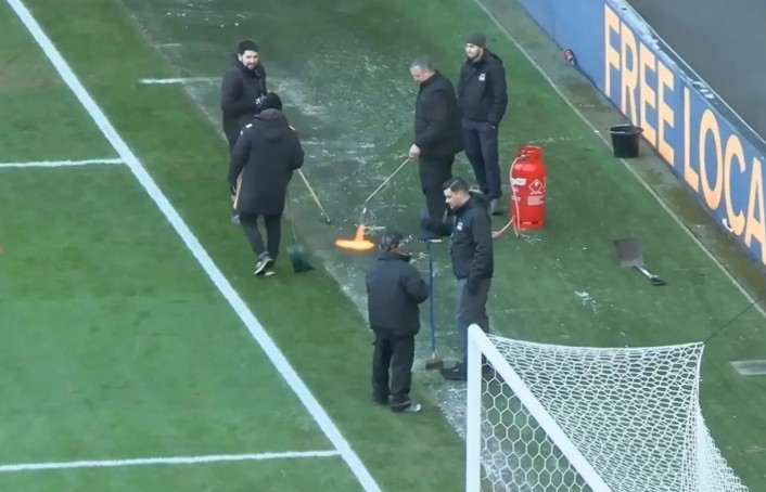 Nhân viên sân bãi dùng đèn khò, cố cứu trận đấu trước giờ bóng lăn.