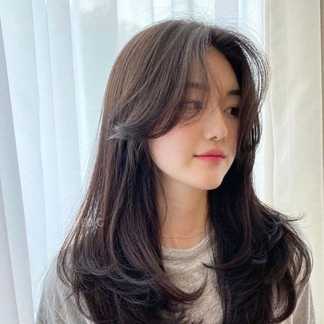 Phần mái được cắt dài, uốn cong nhẹ và ôm sát hai bên má giúp che đi xương hàm hoặc phần gò má rõ, từ đó tạo cảm giác khuôn mặt nhỏ nhắn hơn.